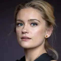 Alicia Agneson, med blå ögon och blont hår uppsatt i en hästsvans, bär en guldig örhänge.