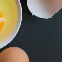 Un huevo crudo en un cuenco blanco, cáscara de huevo rota y dos huevos enteros. Es como soñar con huevos, un festín visual.