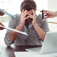 Uomo stressato, sommerso da richieste: tablet, fogli, telefono, matita. Il superlativo di busy è qui.
