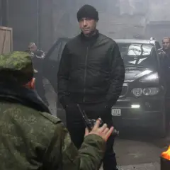 W magazynie, wśród dymu i ognia, mężczyzna w czapce i kurtce bomberce, niczym pitbull, ostatni pies, mierzy z pistoletu do żołnierza.