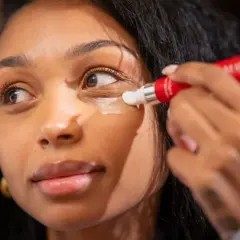 Donna applica crema contorno occhi per contrastare i segni sotto gli occhi, con un tubetto rosso.