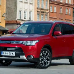 Czerwony Mitsubishi Outlander na tle kamienic. Wiele osób szuka mitsubishi outlander opinie przed zakupem.