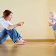 Mamma incoraggia il suo bambino, che sta imparando quando iniziano a camminare i bambini, a fare i suoi primi passi.