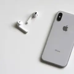 Srebrny iPhone i białe słuchawki AirPods leżą na białym tle. Może rozmówca na iPhonie słabo słychać?