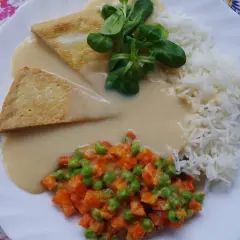 Talerz z ryżem, warzywami i dwoma trójkątnymi kawałkami czegoś w kremowym sosie. Idealny sos do ryżu!