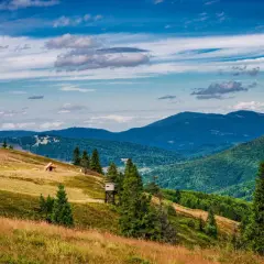 Widok na malowniczą **przełęcz Przegibek** z drewnianą chatką i wieżą widokową na zboczu. W tle gęsto zalesione góry pod błękitnym, chmurnym niebem.