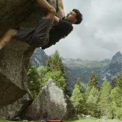 Mężczyzna wspina się po skale w górach, stosując zasady boulderingu. W tle piękne krajobrazy.