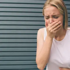 Kobieta z blond włosami zakrywa usta dłonią, czując mdłości. Może to być objaw zatrucia, np. metanolem.