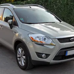 Szary Ford Kuga, SUV, prezentuje swoje wymiary na tle zielonego żywopłotu.