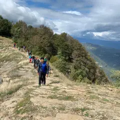 Grupo de excursionistas recorre la ruta puigsacalm, un sendero rocoso con vistas a un valle boscoso bajo un cielo nublado.