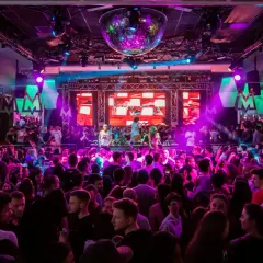 En stor publik njuter av 30 års fest aktiviteter med DJ och discokula. Ljusshow i lila och rosa skapar en festlig stämning.