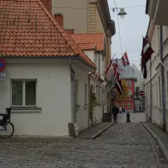 Urokliwa uliczka w Rydze, z łotewskimi flagami i brukowaną nawierzchnią. Idealne miejsce, by poczuć atmosferę miasta i odkryć, co zobaczyć w Rydze.
