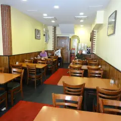 Interiör av en turkisk restaurang i Stockholm. Flera bord med trästolar och röda mattor. Tre gäster sitter vid borden.