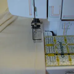 A ruler guides fabric under a coverstitch machine needle, showing how to use a coverstitch machine for precise hemming.