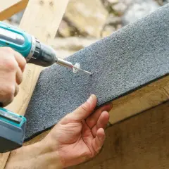 Hand schraubt Dachpappe fest, um Beulen in der Dachpappe zu vermeiden.