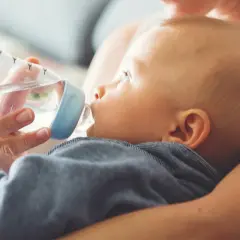 Mama próbuje nakarmić butelką dziecko, które nie chce pić wody.