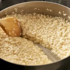 Drewniana łyżka miesza kremowy ryż do risotto w garnku.