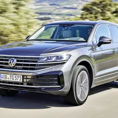 Szary Volkswagen Touareg pędzi po drodze, otoczony zielenią.