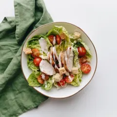Sałatka cezar bez sosu worcestershire: grillowany kurczak, chrupiące grzanki, pomidorki koktajlowe i sałata rzymska polane kremowym dressingiem.