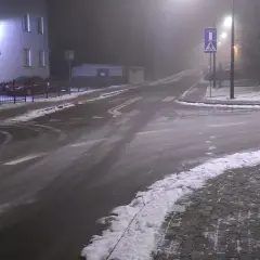 Skrzyżowanie dróg w nocy, z mgłą, śniegiem i znakami drogowymi.