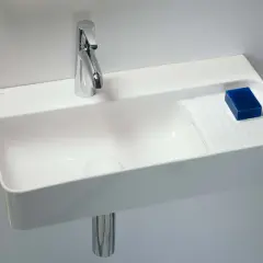 Elegancka, mała umywalka wisząca z chromowaną baterią i kostką niebieskiego mydła.