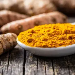 Frisch geschnittene Kurkumawurzeln und leuchtend gelbes Kurkumapulver auf einem Löffel. Die Kurkuma-Eigenschaften sind bekannt für ihre Farbe und ihren würzigen Duft.