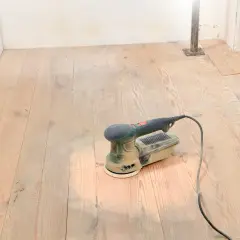 Outil de ponçage bois posé sur un parquet clair, prêt à lisser les planches.