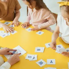 Dzieci ćwiczą pamięć fonologiczną, dopasowując litery na żółtym stole.