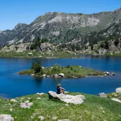 Persona sentada en roca contempla el azul intenso del circ de Colomers, rodeado de montañas verdes y un cielo despejado.