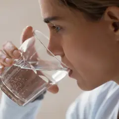 Kobieta pije wodę z kieliszka, wykonując test na odwodnienie.