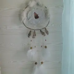 Un attrape rêve, ornement traditionnel, orné d'un loup hurlant, de plumes et de perles, suspendu devant un mur en bois clair.