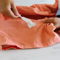 Comment enlever du chewing gum sur un tee shirt : une spatule blanche applique une pâte sur une tache de chewing gum sur un tissu corail.