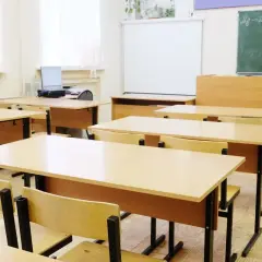 Pusta klasa szkolna z rzędami drewnianych ławek i krzeseł, tablicą i projektorem.