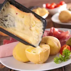Une idée raclette originale : du fromage fondu coulant sur des pommes de terre, charcuterie et cornichons.