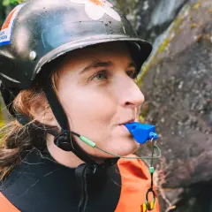 Persona con casco y traje naranja sopla un silbato de emergencia azul, listo para cualquier aventura acuática.