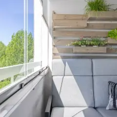 Przytulna loggia z szarą sofą, poduszką z liskiem i zielenią na drewnianej ściance.