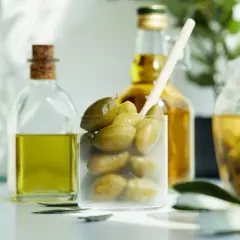 Zielone oliwki w szklance, obok butelki oliwy. Zastanawiasz się nad oliwki kcal?