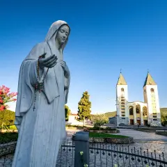 Pomnik Matki Bożej z różańcem przed kościołem w Medziugorie. Planujesz podróż? Dowiedz się, jak dolecieć samolotem do Medziugorie.