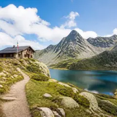 Sentier de randonnée en Andorre menant à un refuge de montagne près d'un lac alpin aux eaux bleues, avec des montagnes escarpées en arrière-plan.
