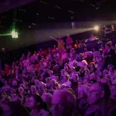 Publik njuter av en konsert i Uppsala. Scenen badar i lila ljus, och en artist gestikulerar mot publiken.