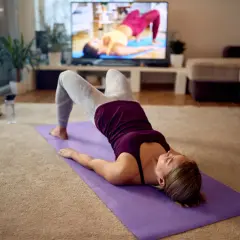 Mujer haciendo ejercicio en casa, buscando algo para el estreñimiento. Yoga en la alfombra frente a la TV.