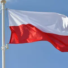 Biało-czerwona bandera flaga Polski powiewa na maszcie na tle błękitnego nieba.