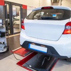 Controllo emissioni per la revisione auto scaduta. Un'auto bianca è collegata a un analizzatore di gas di scarico in un'officina.
