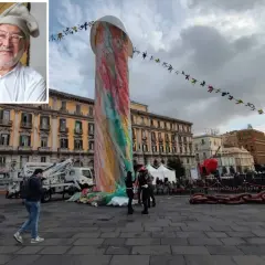 Ritratto di artista con inquadratura di una colorata statua di Pulcinella a Napoli, in piazza, con edifici storici sullo sfondo.