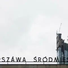 Varso Tower w budowie z dźwigami, na tle napisu "WARSZAWA ŚRÓDMIEŚCIE".