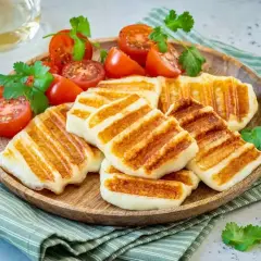 Grillowany ser halloumi na drewnianej tacy, podany z pomidorkami koktajlowymi i świeżą kolendrą. Idealny na letnie przekąski.