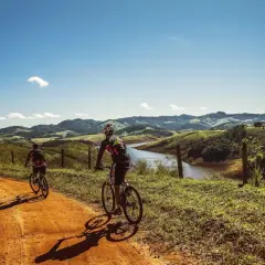 Dwóch rowerzystów przemierza malownicze trasy rowerowe w górach, podziwiając krajobraz z jeziorem i pagórkami.