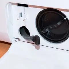 Otwarta klapka z wężykiem do spuszczania wody i czarną zakrętką filtra. Dowiedz się, jak wyczyścić filtr w pralce Whirlpool, aby zapewnić jej sprawność.
