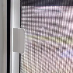 Moskitiera na okno z roletą zewnętrzną, chroniąca przed owadami. Widoczny metalowy zatrzask i biała rączka.