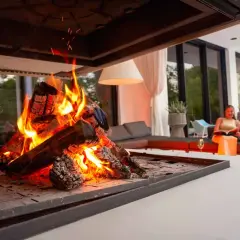 En kvinna läser en bok vid en brasa med elda granved.
